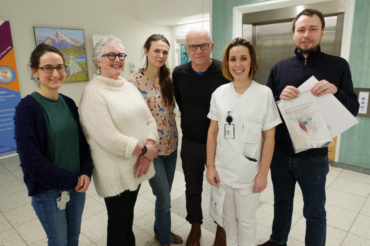 Seks smilende mennesker poserer i en sykehusgang.