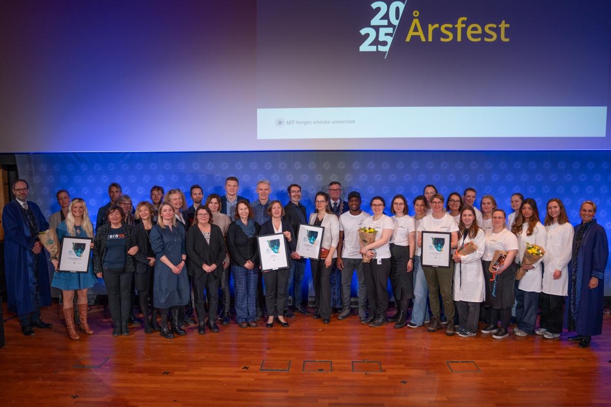 en gruppe p&aring; rundt 20 mennesker fremst i et auditorium, flere med blomster og diplom