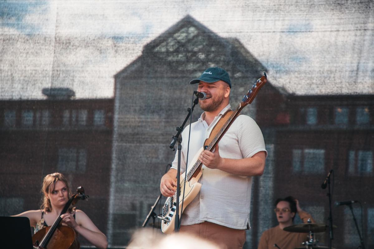 Mannlig vokalist med caps og gitar på campus-scene