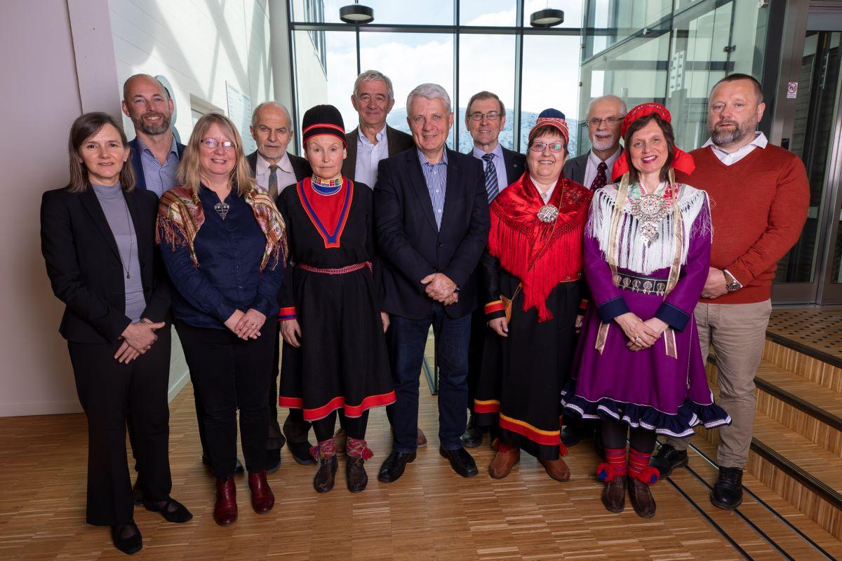 En gruppe mennesker, noen i dress, noen i kofte, poserer i en trapp