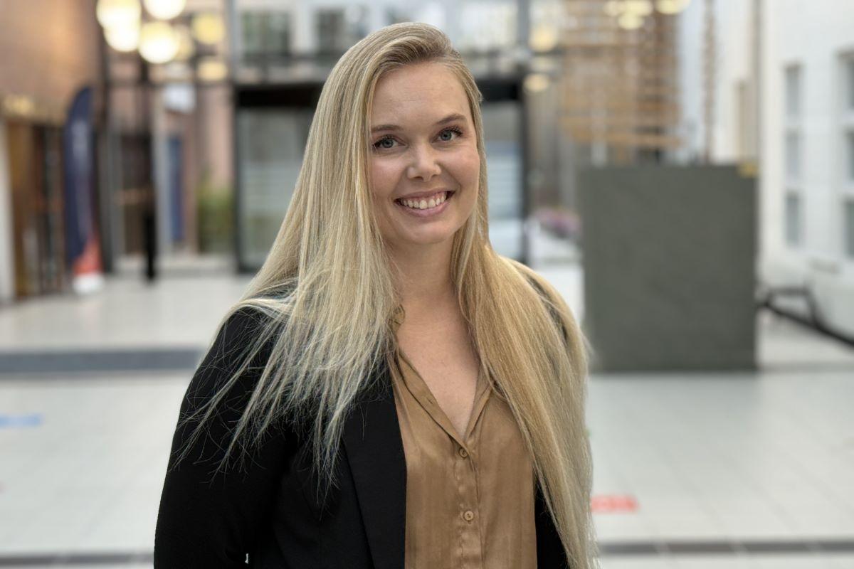 Blond kvinne smiler i kamera, uklar bakgrunn