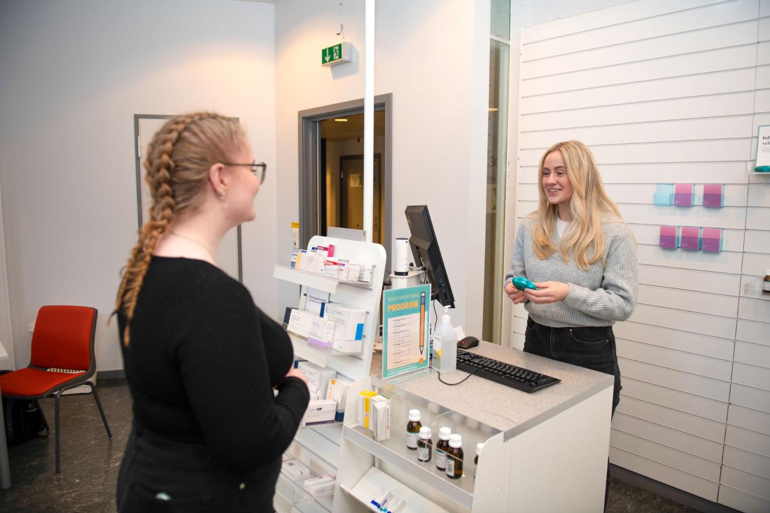 Farmas&oslash;yt som st&aring;r bak kassen p&aring; et apotek og prater med en kunde.