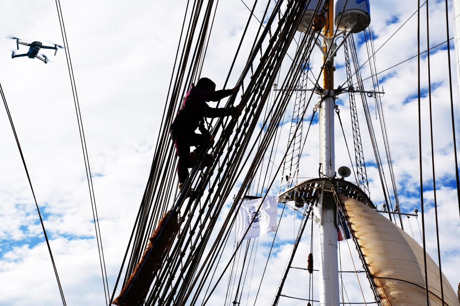 Person klatrer opp skipsmast med drone i bakgrunn