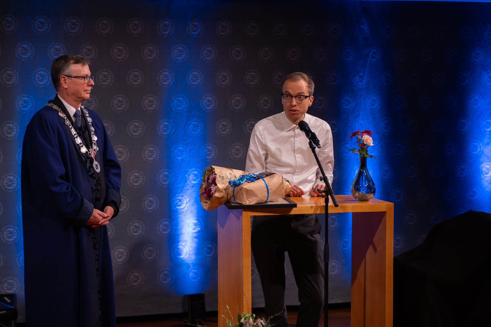 Mann mottar diplom, blomster og gave i staselig og feststemt universitetsauditorium. 